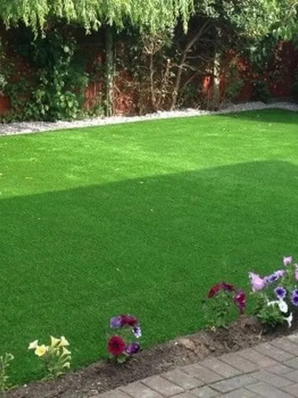 A classic, beautiful backyard lawn created with high-quality artificial turf. It stays perfectly green and manicured next to the flower beds and brick pavers, providing a flawless look all year.