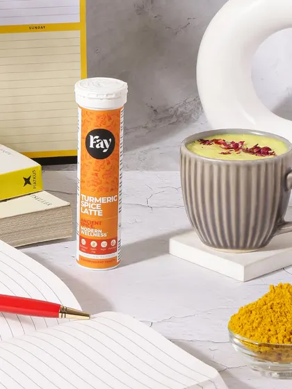 This image styles a turmeric spice latte supplement in a desk setting. The open notebook and pen position it as a drink that aids focus and productivity during a workday.