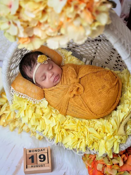 A newborn rests in a hanging chair prop decorated with yellow flowers. The calendar block marks the special day, adding a personal touch to the portrait.