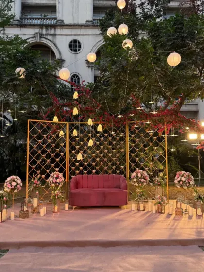 A cozy and romantic outdoor seating area. We designed this photo booth with a pink sofa, a golden lattice backdrop, and an array of candles and hanging lights for a magical evening ambiance.