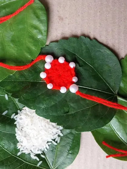 A red crochet rakhi with white pearl-like beads. A simple, traditional color combination.