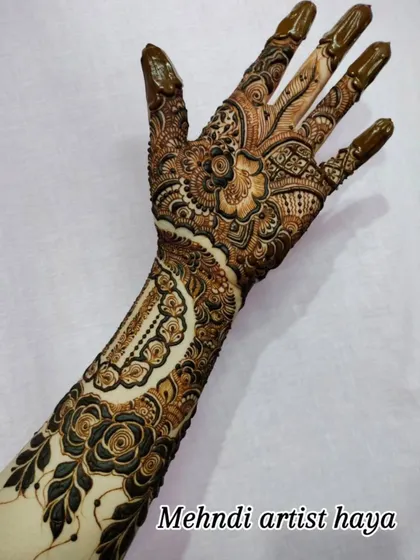 The full design, with the henna paste still on, showing the contrast between the dark paste and the skin. This piece combines bracelet and hand jewelry concepts.