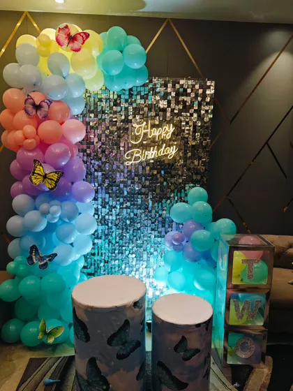 A beautiful butterfly theme with a silver shimmer wall. The pastel rainbow balloon arch is accented with butterfly cutouts, creating a magical photo spot.