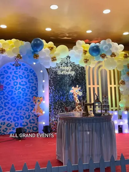 A wide view of the stage, showing the cake table placed centrally in front of the jungle-themed backdrop with a shimmer wall accent.