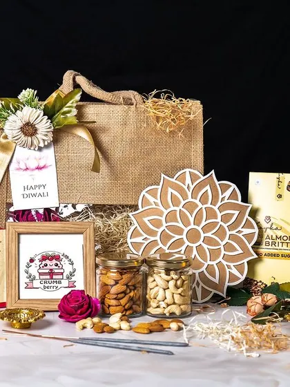 This professionally shot image highlights a beautiful Diwali hamper featuring a jute bag, a box of sweets, cookies, a decorative mandala, and jars of nuts. It's a perfect example of a balanced gift that combines traditional and contemporary elements.