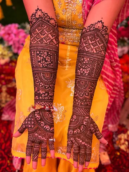 A beautiful shot of full bridal mehndi against a colorful wedding backdrop. The design features traditional architecture and intricate filler patterns.