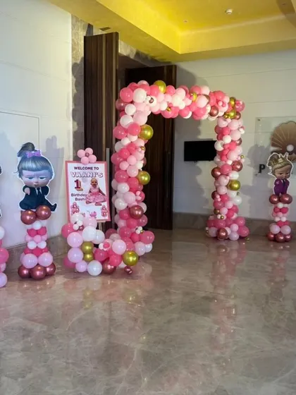 An entrance arch for a Boss Baby themed first birthday party, featuring pink and gold balloons and character cutouts.
