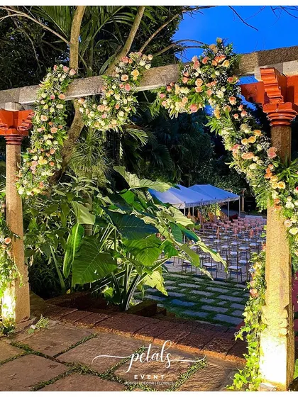 A stone entrance arch is adorned with whimsical spiral flower bunches and delicate ivy leaves, creating a magical and unique welcome for guests.
