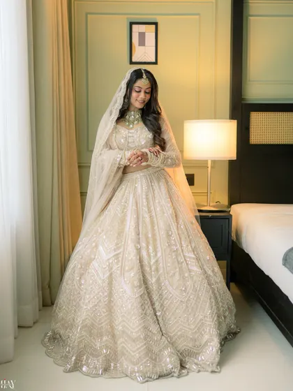 A full-length portrait of the bride in her stunning white lehenga, getting ready in her hotel room.