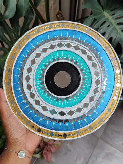 A 10-inch evil eye inspired Lippan art piece. The concentric circles of blue, white, and gold with mirror work are believed to offer protection and bring good luck.
