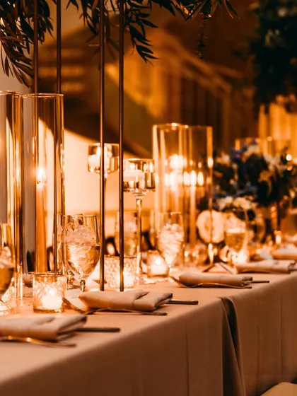 A close-up of an elegant tablescape. The warm candlelight, tall glass vases, and minimalist floral arrangements create an intimate and luxurious dining experience for guests.