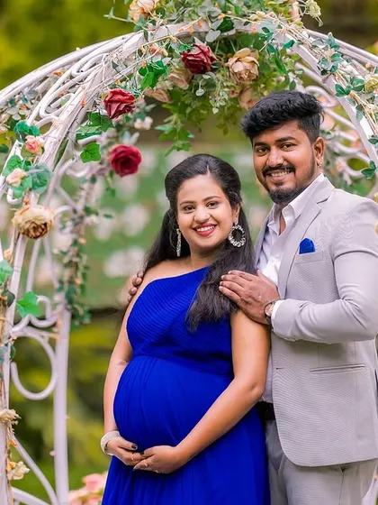 A close-up portrait of the couple standing by a white floral carriage prop. The soft colors of the flowers and the romantic setting make this a perfect shot for a fairy tale themed maternity shoot.