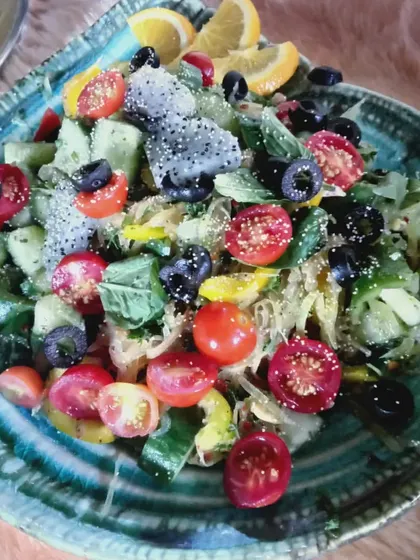 A Greek-inspired salad with cucumber, cherry tomatoes, and black olives, topped with what appears to be dragon fruit.