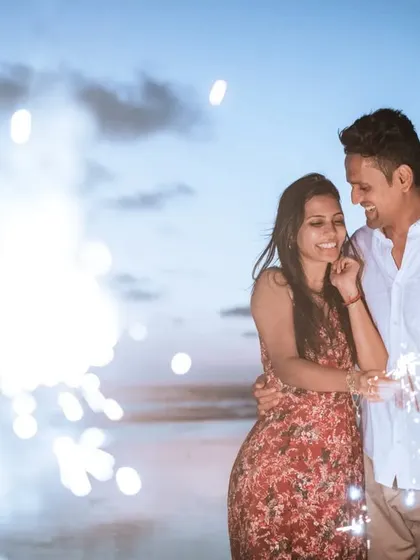 A happy, candid moment between a couple celebrating with sparklers on the beach at dusk.