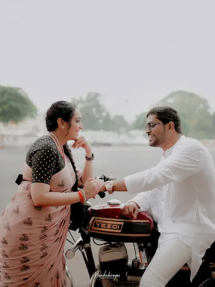 A couple shares a lighthearted moment, leaning against a vintage Yezdi motorcycle in Mysore. This shot combines personal interests with a classic pre-wedding theme.