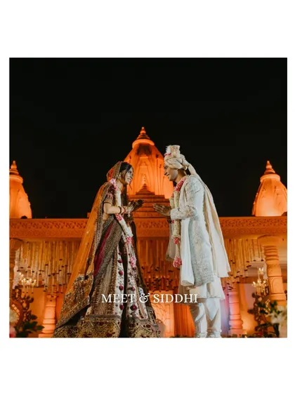 A candid moment during the varmala ceremony, capturing the couple's interaction and the stunning architectural backdrop. The focus is on their shared glance and the beginning of their life together.