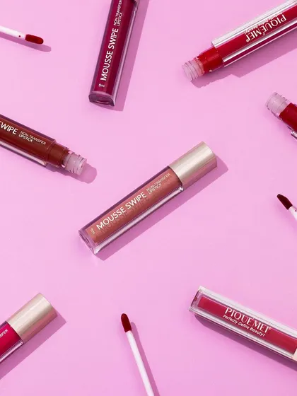 This flatlay of PiqueMei lipsticks showcases the variety of shades in a playful, scattered arrangement. The top-down perspective is perfect for social media and gives a clear view of the product applicators and colors.