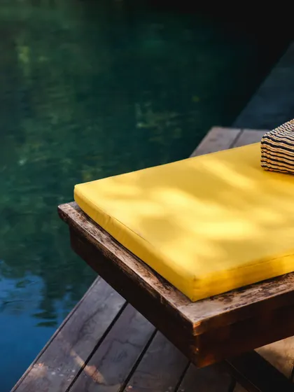 A simple, abstract shot of the yellow lounger cushion next to the deep green water of the pool.