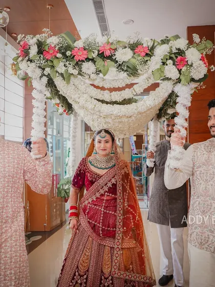 A classic bridal entry, elevated with a lush floral chaadar. The canopy of white flowers and pearls adds a touch of grace and tradition as the bride makes her way to the ceremony.