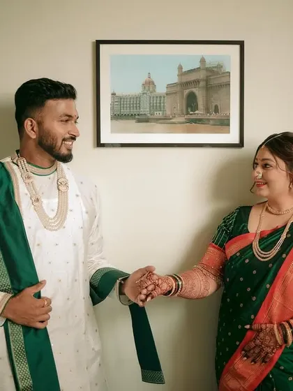 A lovely indoor portrait of the couple holding hands, with a framed picture of the Taj Mahal Palace Hotel adding a touch of Mumbai to their wedding story.