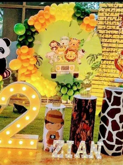 A safari-themed second birthday party. The decor includes a large marquee number '2', various animal cutouts like a panda and tiger, and a balloon arch in jungle colors.