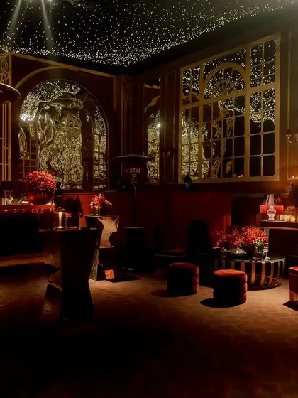 A view of the lounge area, showing the intricate gold-leafed backdrops and mirrored panels. The space is bathed in a warm, red glow, creating a luxurious and intimate atmosphere for guests.
