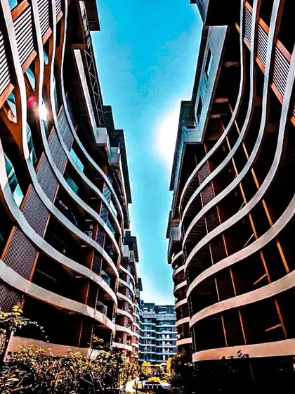An upward view of the Palm Bellagio's wave-inspired facade in Raipur. The flowing curves of the balconies create a sense of movement, breaking the monotony of a typical residential block and establishing a unique architectural identity.