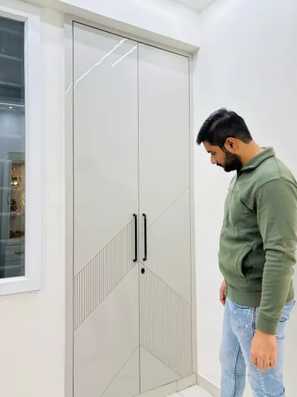 This hinged wardrobe design uses a combination of high-gloss laminate and textured grooves for a modern look. The clean lines and simple black handles make it a stylish addition to the bedroom.