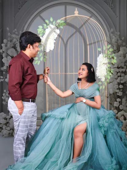 A playful and sweet interaction in our birdcage prop. The mom-to-be sits elegantly in a teal gown while her partner stands beside her, sharing a moment.