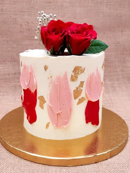 We celebrate romance with the classic beauty of red roses. Fresh, vibrant red roses sit atop a simple white cake, which is artfully decorated with abstract brushstrokes of red and pink buttercream and flecks of gold leaf for a modern, artistic touch.