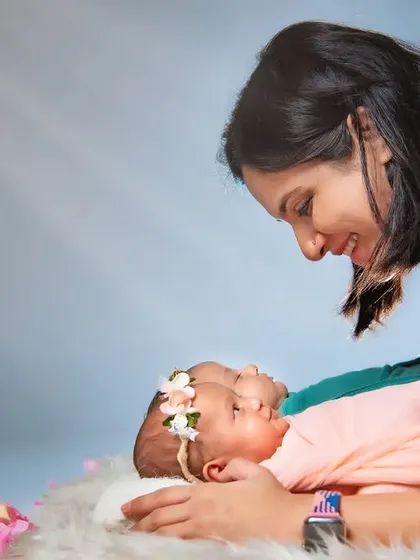 A mother gazes lovingly at her twin newborn daughters. The soft lighting and gentle pose create a serene and angelic atmosphere for this special twin photoshoot.
