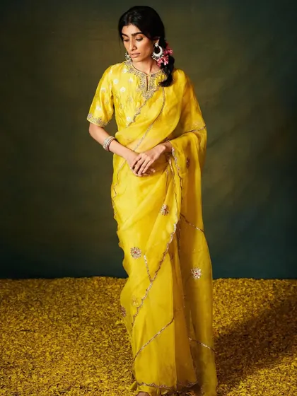 Sunshine yellow in sheer organza. This saree is detailed with a scalloped silver border and delicate floral embroidery, making it a cheerful and elegant choice for a Haldi ceremony or a daytime event.