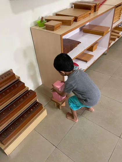 A child works with the Pink Tower, a classic sensorial material. This activity helps them visually discriminate between sizes and builds their understanding of dimensions, which is an indirect preparation for mathematics.