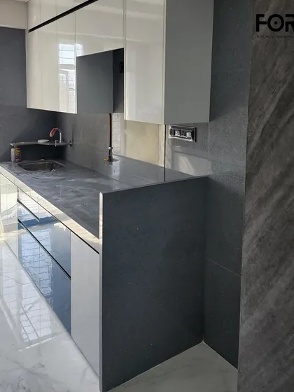 A simple yet elegant L-shaped kitchen layout with glossy white cabinets and a dark grey countertop that extends up as a partial backsplash. This minimalist design is perfect for smaller, modern homes.