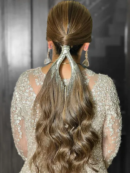 A unique and modern ponytail hairstyle, perfect for a cocktail or reception party. The hair is wrapped with a silver accessory for a chic finish.