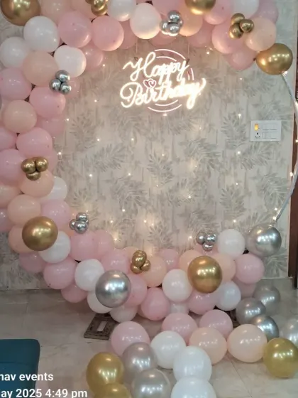 A lovely birthday backdrop with a circular frame and a balloon garland in pastel pink, white, and gold. The 'Happy Birthday' neon sign and fairy lights create a warm and inviting atmosphere.