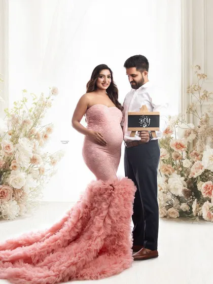 A lovely gender reveal photo. The couple stands amidst a beautiful floral setup as they announce 'It's a boy' with a small chalkboard sign, adding a personal touch to the session.