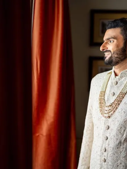 A close-up portrait of the groom looking out the window with a happy smile. The soft light highlights his features and the joy in his eyes.