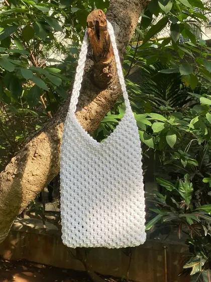 Our white macrame shoulder bag hanging in natural light. This shot showcases its simple, clean lines and handmade quality.