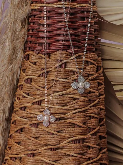 A close-up of two pearl and diamond clover necklaces against a woven basket. This styling gives the product a rustic yet elegant feel, showing versatility for an online shop.