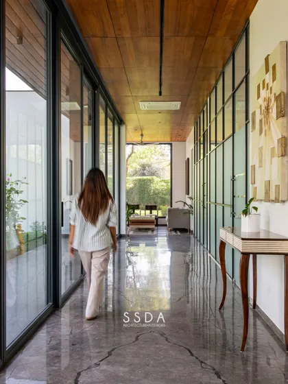 In 'The Green Axis' office, a linear corridor doubles as a contemplative lounge space. The design is intentionally minimal, with a wooden ceiling and glass walls that frame views of the courtyard, promoting a sense of calm and focus.