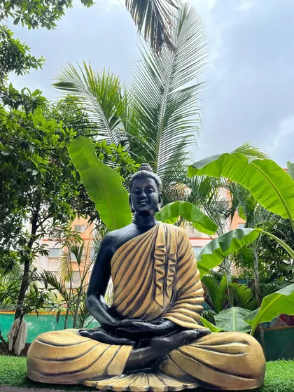 A full-size Gautam Buddha sculpture designed for an outdoor garden space. Made from weather-resistant fiber, the statue's black and gold finish contrasts beautifully with the surrounding greenery.