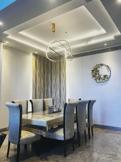 For this dining area, the goal was to create a space that feels both grand and intimate. The multi-layered tray ceiling with concealed lighting adds architectural depth, while the modern sculptural chandelier serves as a stunning centerpiece. The combination of a marble-top table, plush upholstered chairs, and subtle wall textures results in a luxurious setting for family meals.