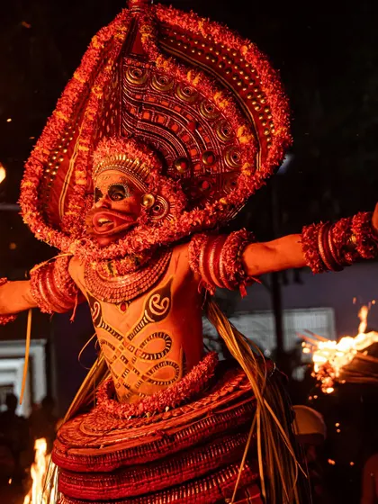 Close-up and action shots of the Kandanar Kelan Theyyam, focusing on the detailed costume, expressive mask, and the raw power of the fire performance.