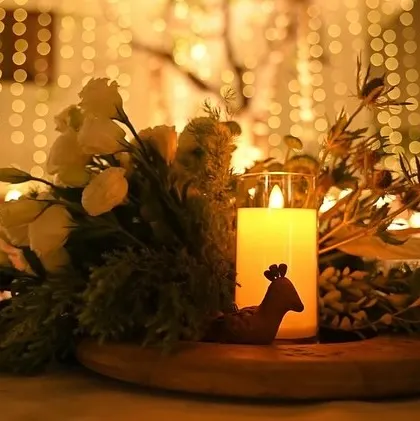 A rustic centerpiece on a wooden platter. The candle's glow silhouettes a small deer figurine, creating a charming and whimsical woodland scene.