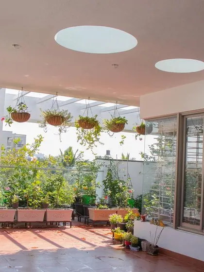 A sun-drenched terrace at 'Isha-Vaasyam', featuring circular skylights and a pergola that supports a lush collection of hanging plants, creating a vibrant urban garden.