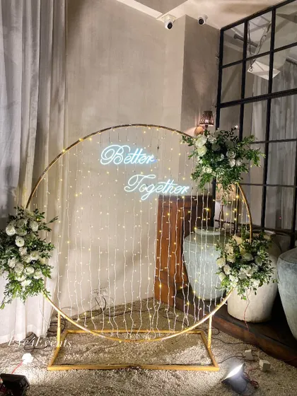 Simple, modern, and elegant. This engagement decor features a large golden ring with a "Better Together" neon sign and cascading fairy lights, flanked by arrangements of classic white flowers.