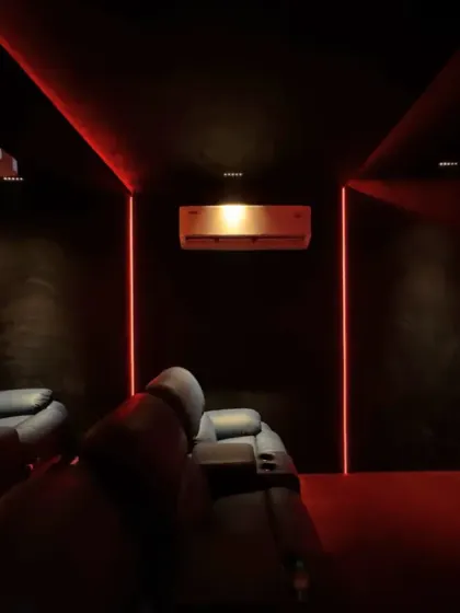 An immersive home theater experience with plush leather recliners, a large projection screen, and dramatic red ambient lighting that sets the mood for movie night.