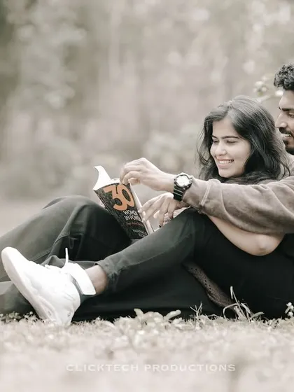 A relaxed and happy moment of a couple sitting in the grass, reading a book together, perfect for a casual, lifestyle pre-wedding shoot.