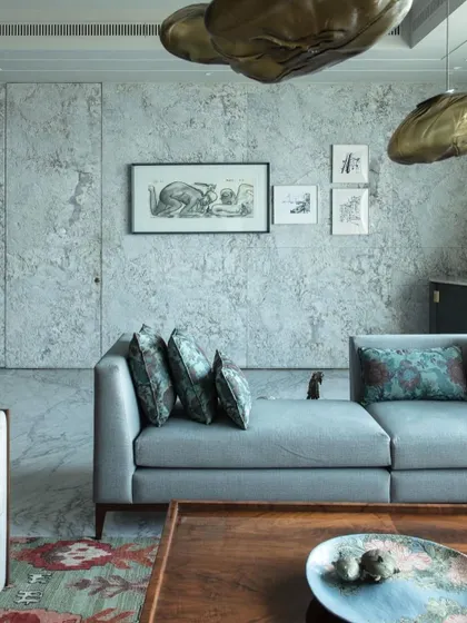 A view of the living room with its textured stone wall and camouflaged door, demonstrating our principle of integrating functional elements seamlessly into the design. The space is curated with art and custom furniture.